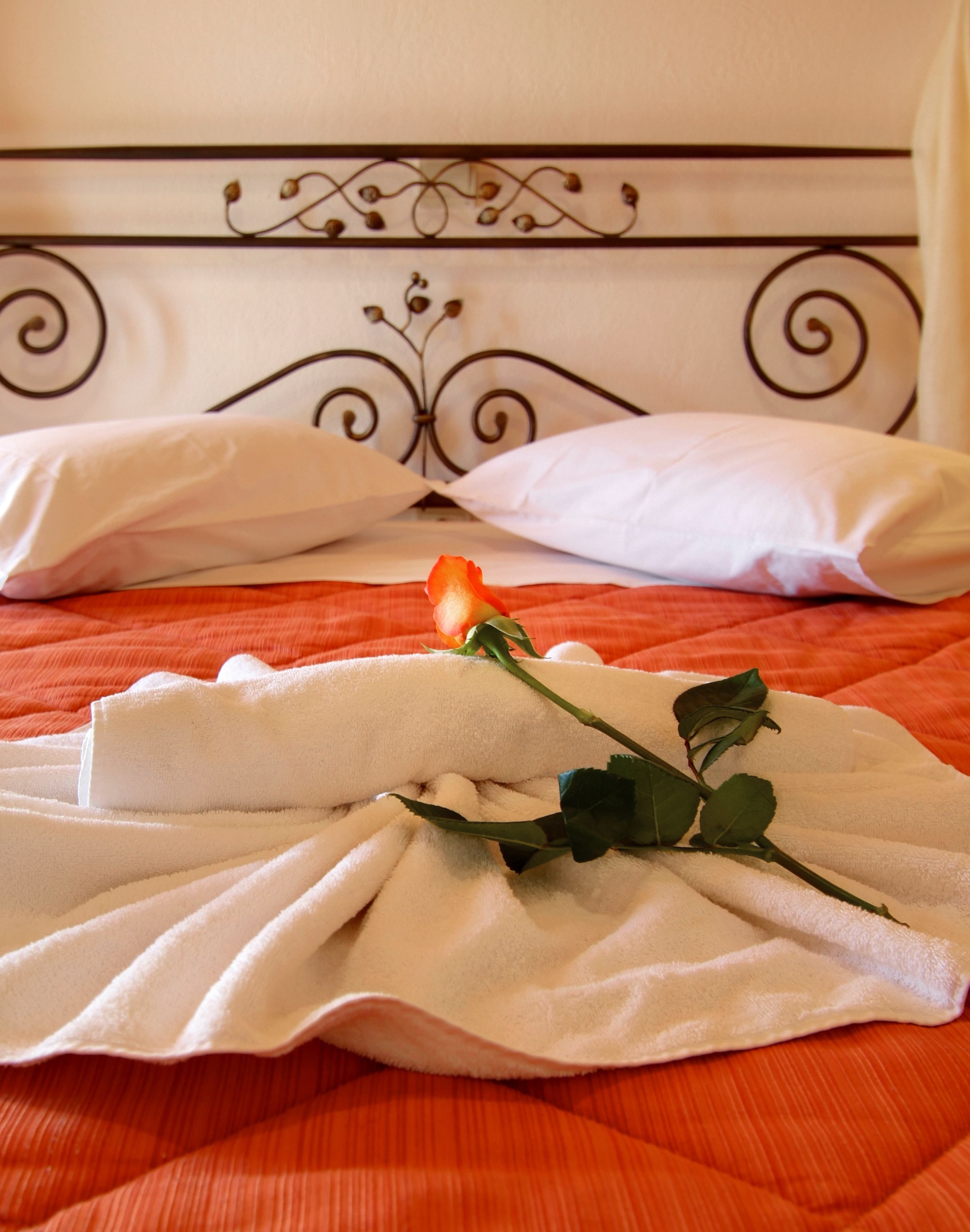 A bed with a white headboard, a rose, and folded towels.