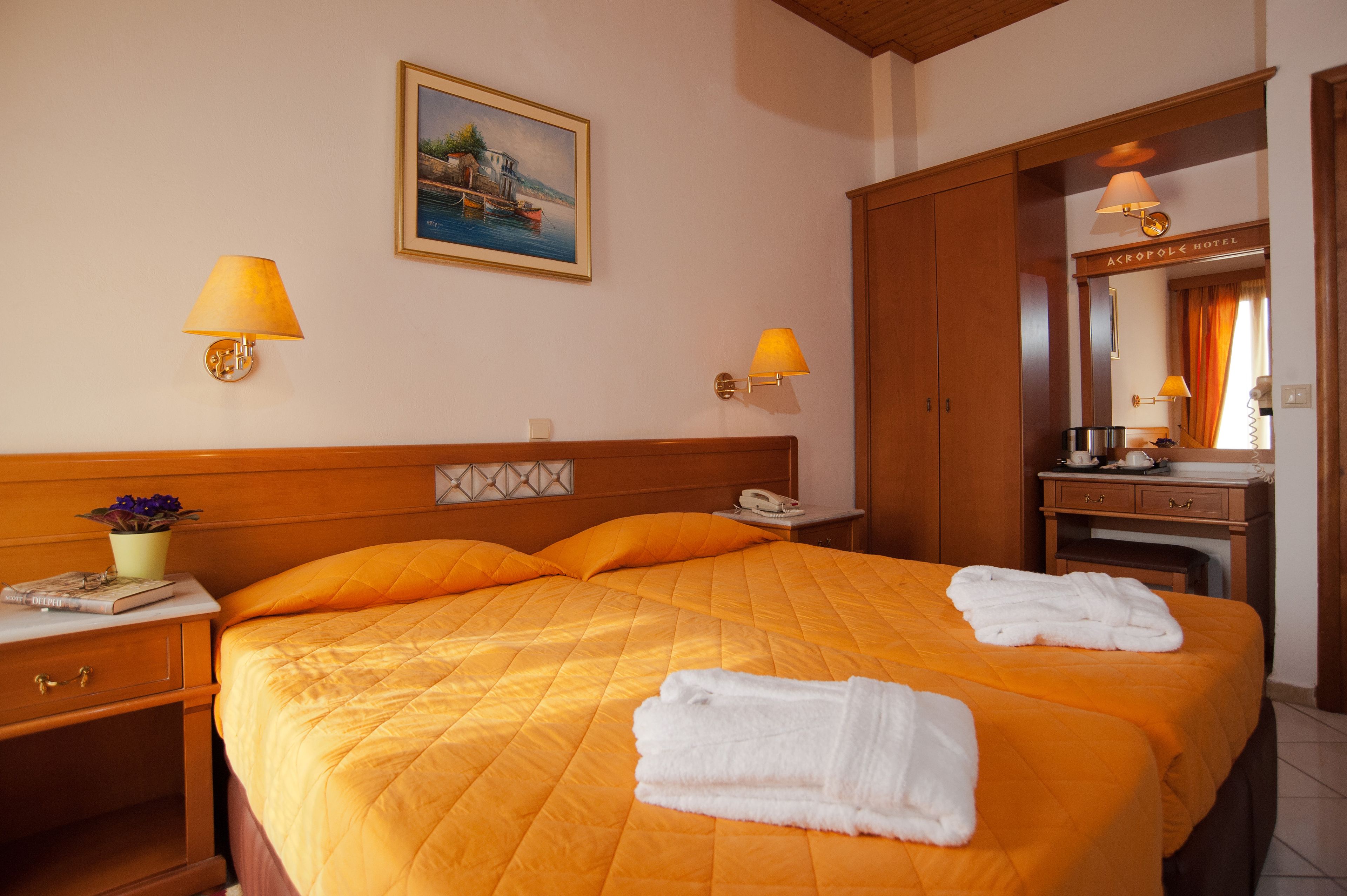 Une chambre d’hôtel avec un grand lit, deux lampes de chevet, un tableau au mur, un bureau avec un téléphone et un miroir sur lequel est accrochée une pancarte.