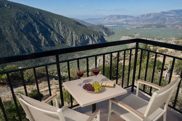 A balcony with a table set for two, a bottle of red wine, a bowl of grapes, and a cheese board. - Acropole Delphi (Delphi)