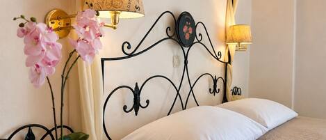A hotel room with a bed, a bedside table with a lamp, a potted plant, and a decorative headboard.