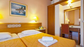 A hotel room with two beds, a wooden headboard, a painting of a coastal scene, a desk with a chair, and a mirror.