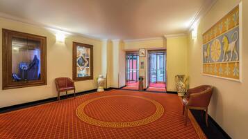 Un vestíbulo de hotel con una alfombra roja estampada, un jarrón grande y una obra de arte enmarcada en la pared.