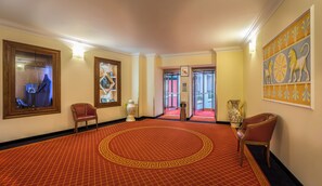 A hotel lobby with a red patterned carpet, a large vase, and a framed artwork on the wall.