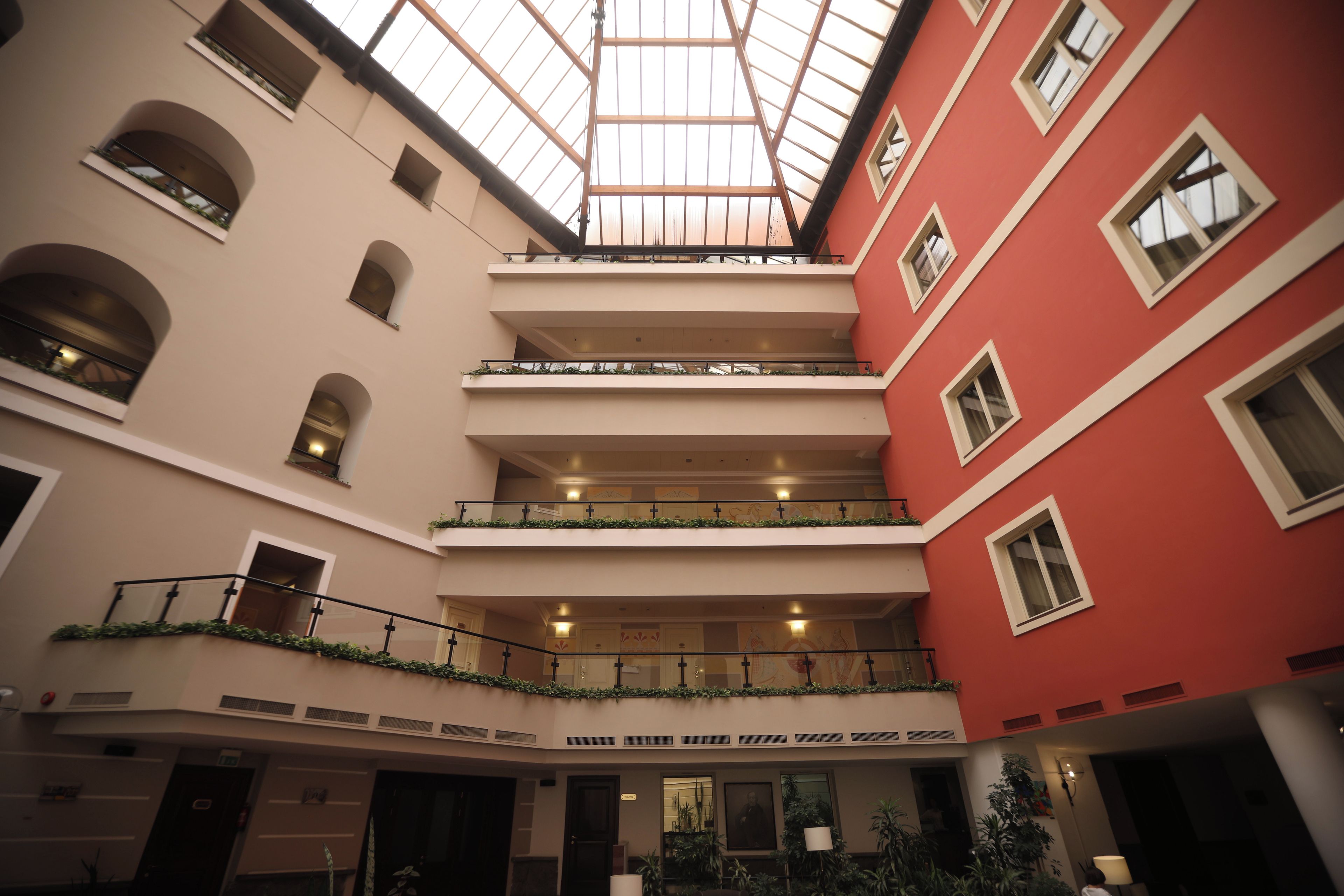 Un atrio a più livelli con soffitto in vetro, balconi con ringhiere e un mix di stili architettonici.