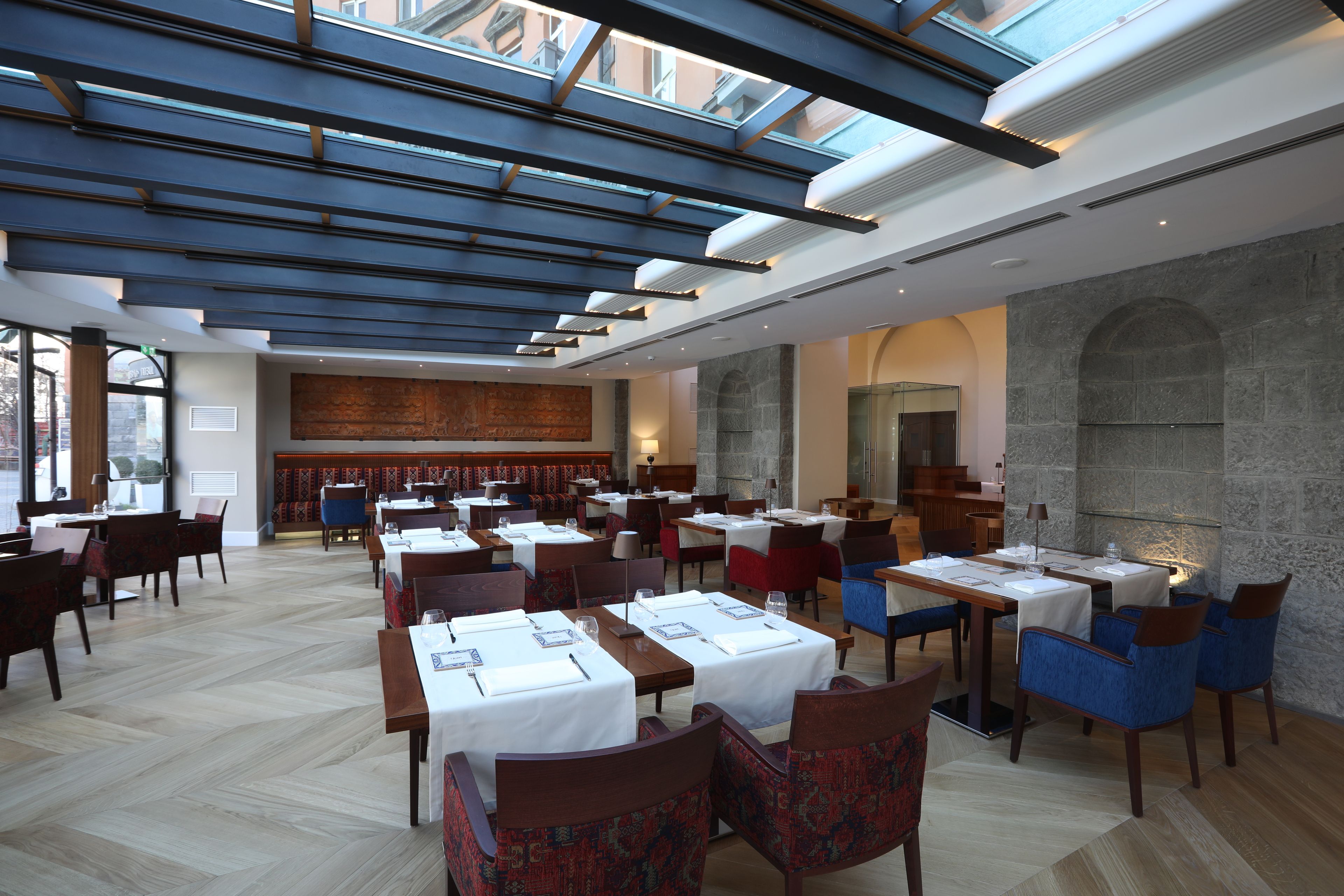 A restaurant with multiple tables and chairs, a stone wall, and a skylight.