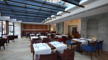 A restaurant with multiple tables and chairs, a stone wall, and a skylight.