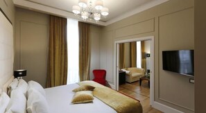 A hotel room with a large bed, a television, a red chair, and a view of the adjacent room. - Grand Hotel Yerevan (Yerevan)