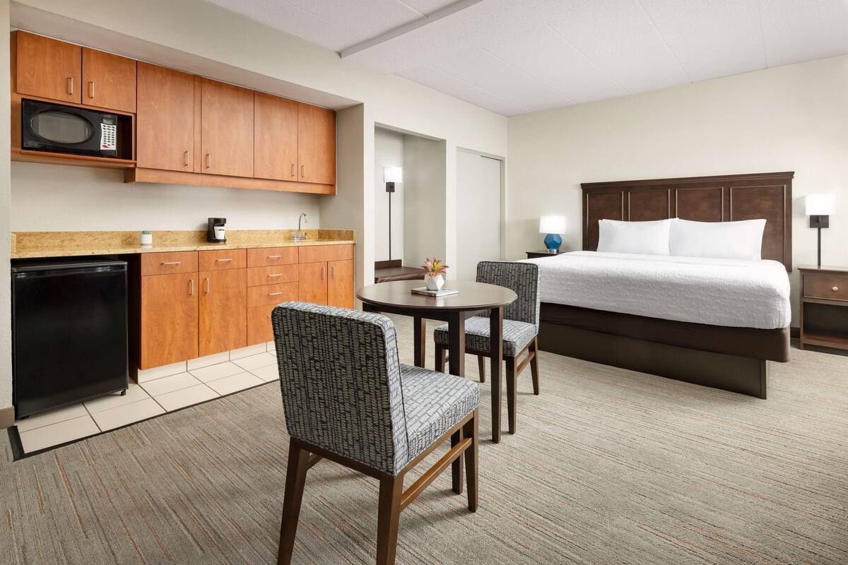 A hotel room with a bed, a desk, a microwave, and a refrigerator.