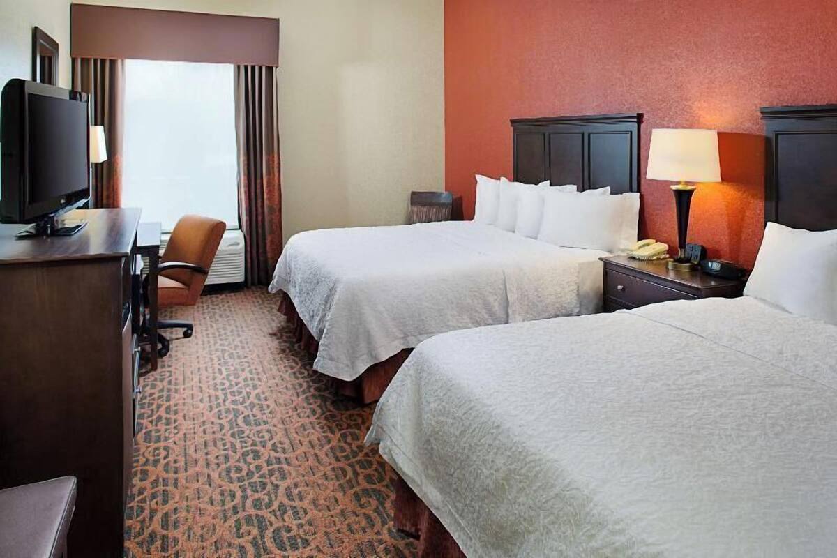 A hotel room with two beds, a desk with a computer, a chair, a lamp, and a telephone.