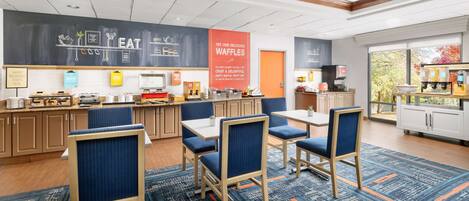 A breakfast area with seating, a chalkboard menu, and a waffle display.