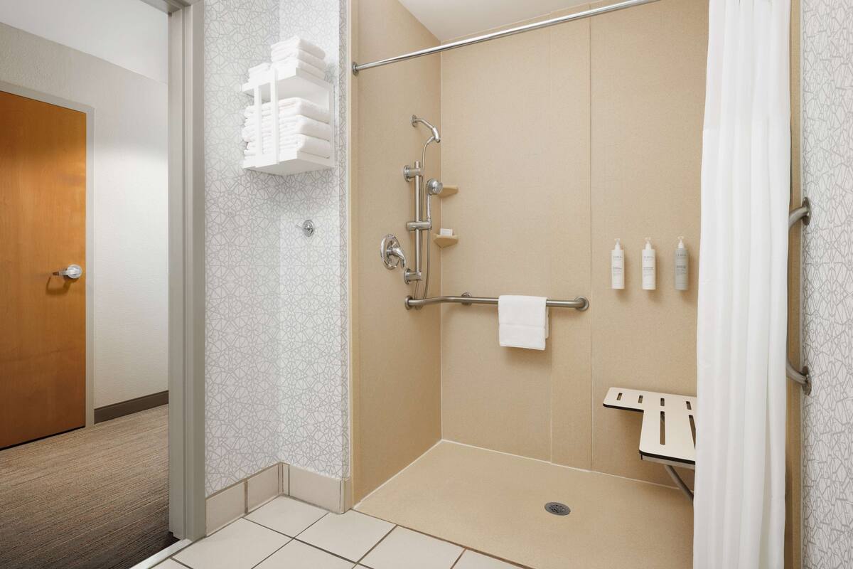 A hotel bathroom with a walk-in shower, a towel rack, and a shelf with toiletries.
