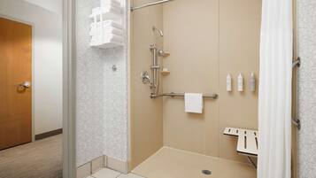 Ein Hotelbad mit barrierefreier Dusche, Handtuchhalter und Ablagefläche für Toilettenartikel.