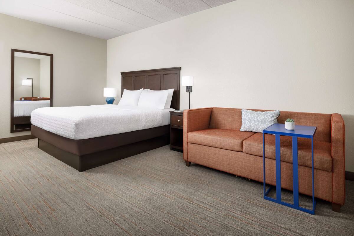 A hotel room with a large bed, a sofa, a small table, and a nightstand.