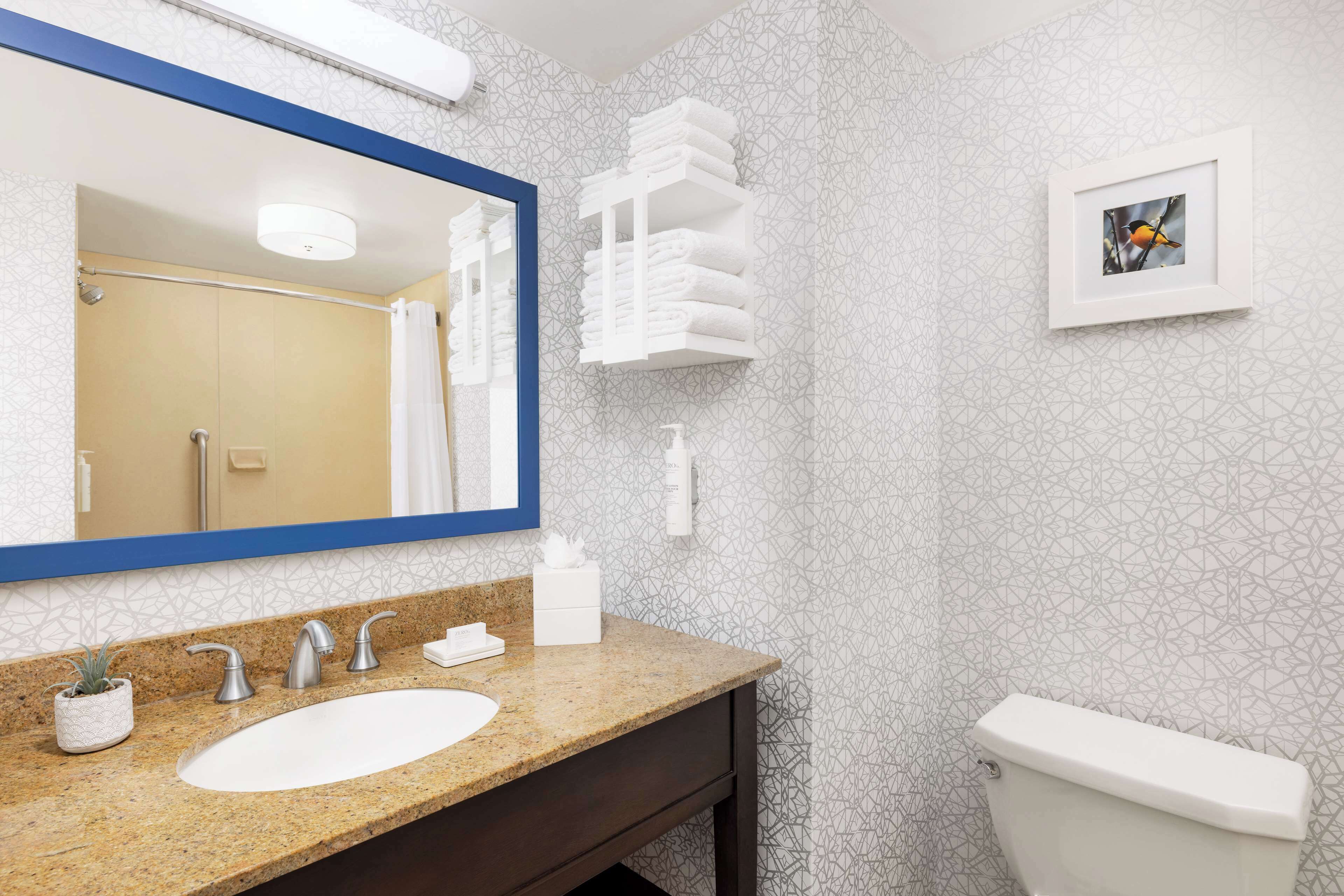 A bathroom with a granite countertop, a white sink, a large mirror, a towel rack, and a toilet.