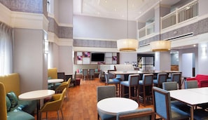 A spacious hotel lobby with multiple seating areas, including round tables and booths, and a large television screen. - Hampton Inn & Suites Atlanta Airport North I-85 (Atlanta)