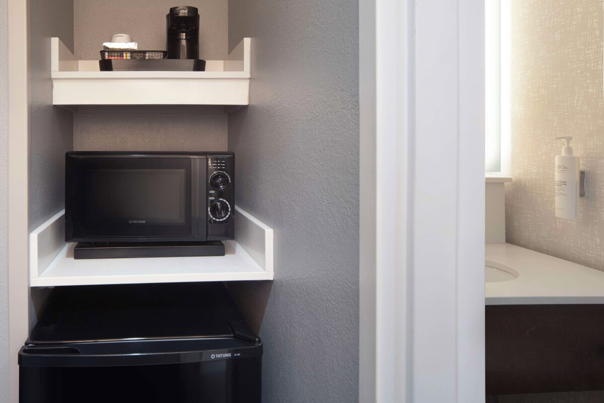A compact kitchen with a microwave, coffee maker, and a trash bin.
