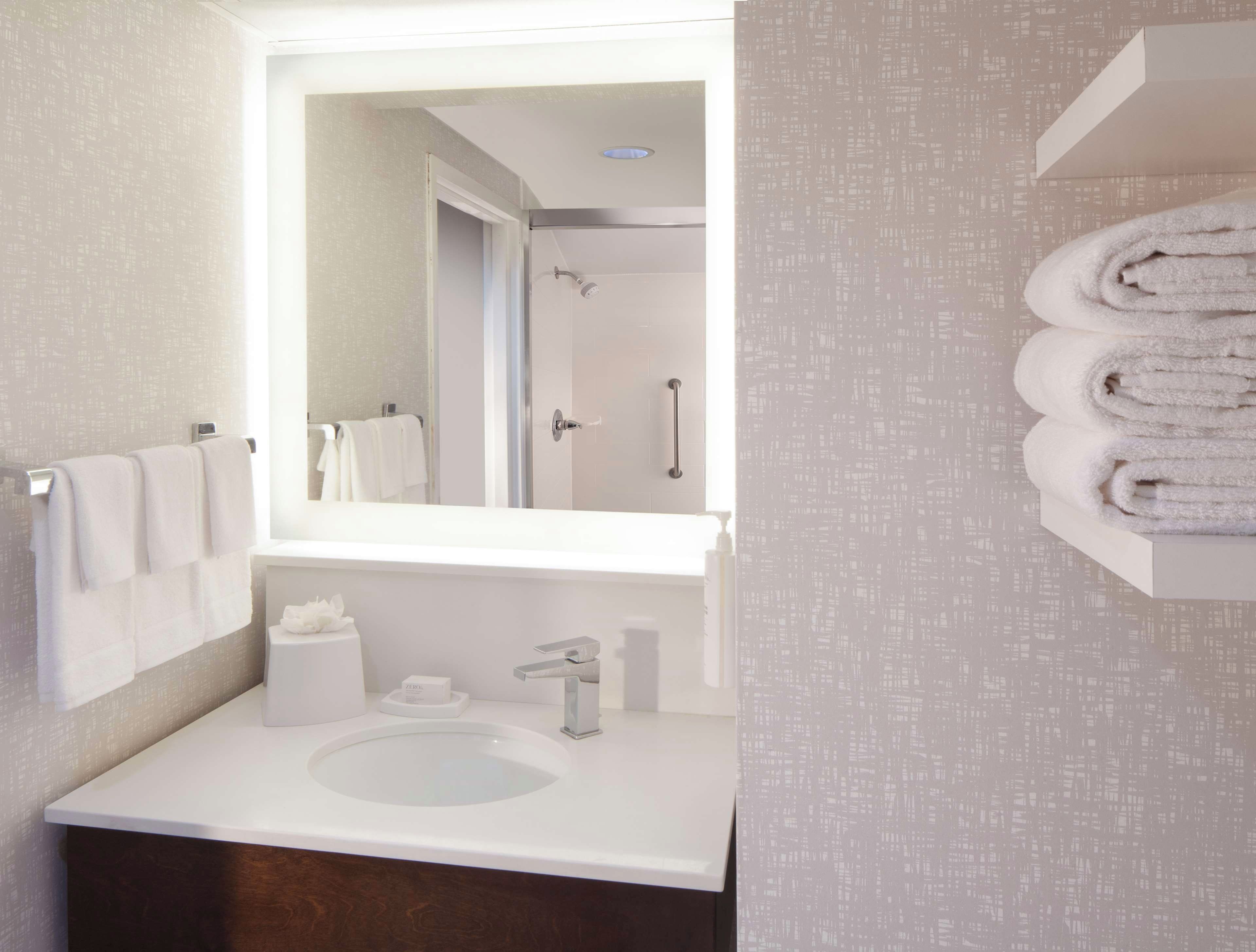 A bathroom with a sink, mirror, towel rack, and a shower area.