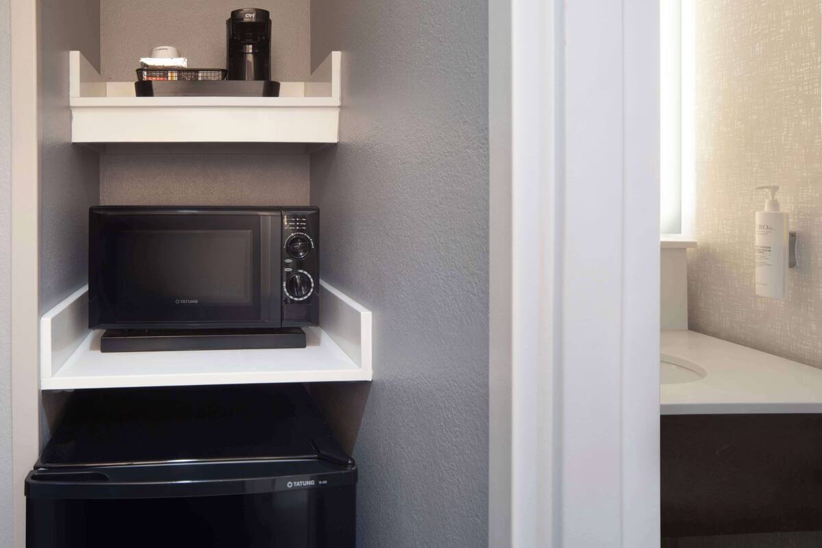 A compact kitchen with a microwave, coffee maker, and a trash bin.