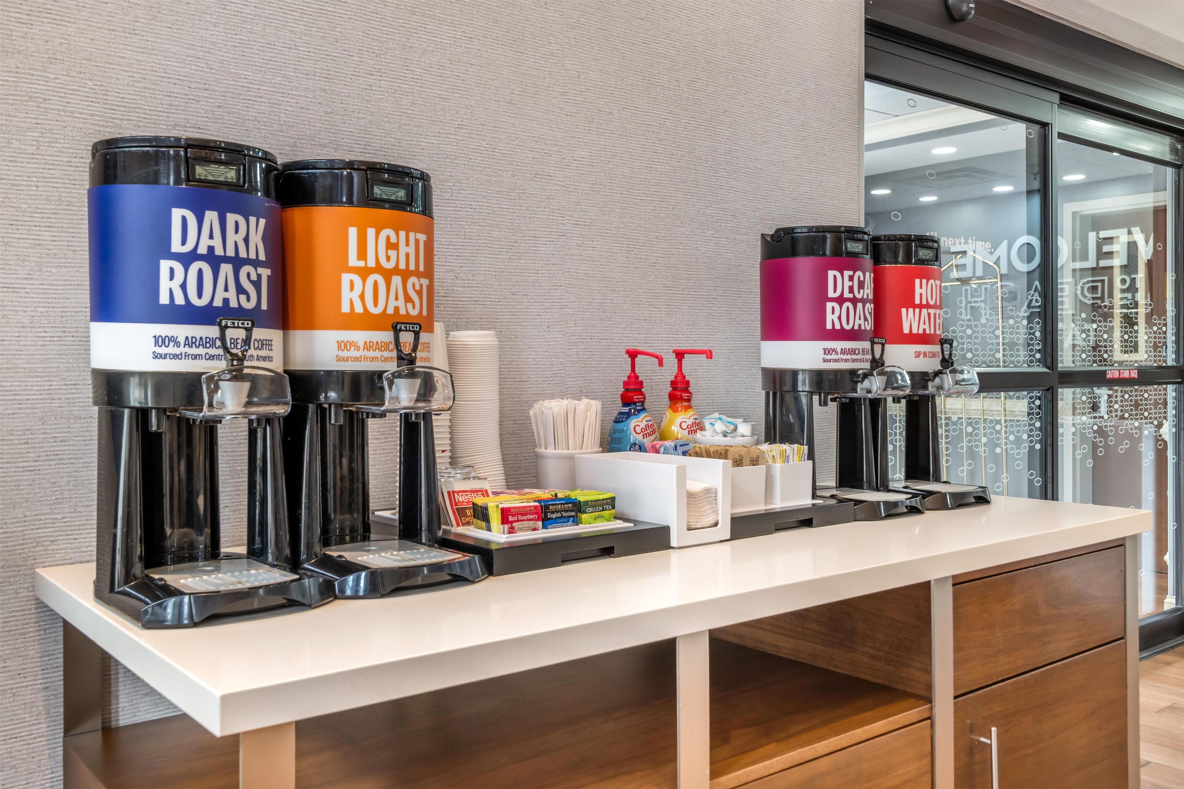 A coffee station with self-service dispensers for dark and light roast coffee, and hot water.