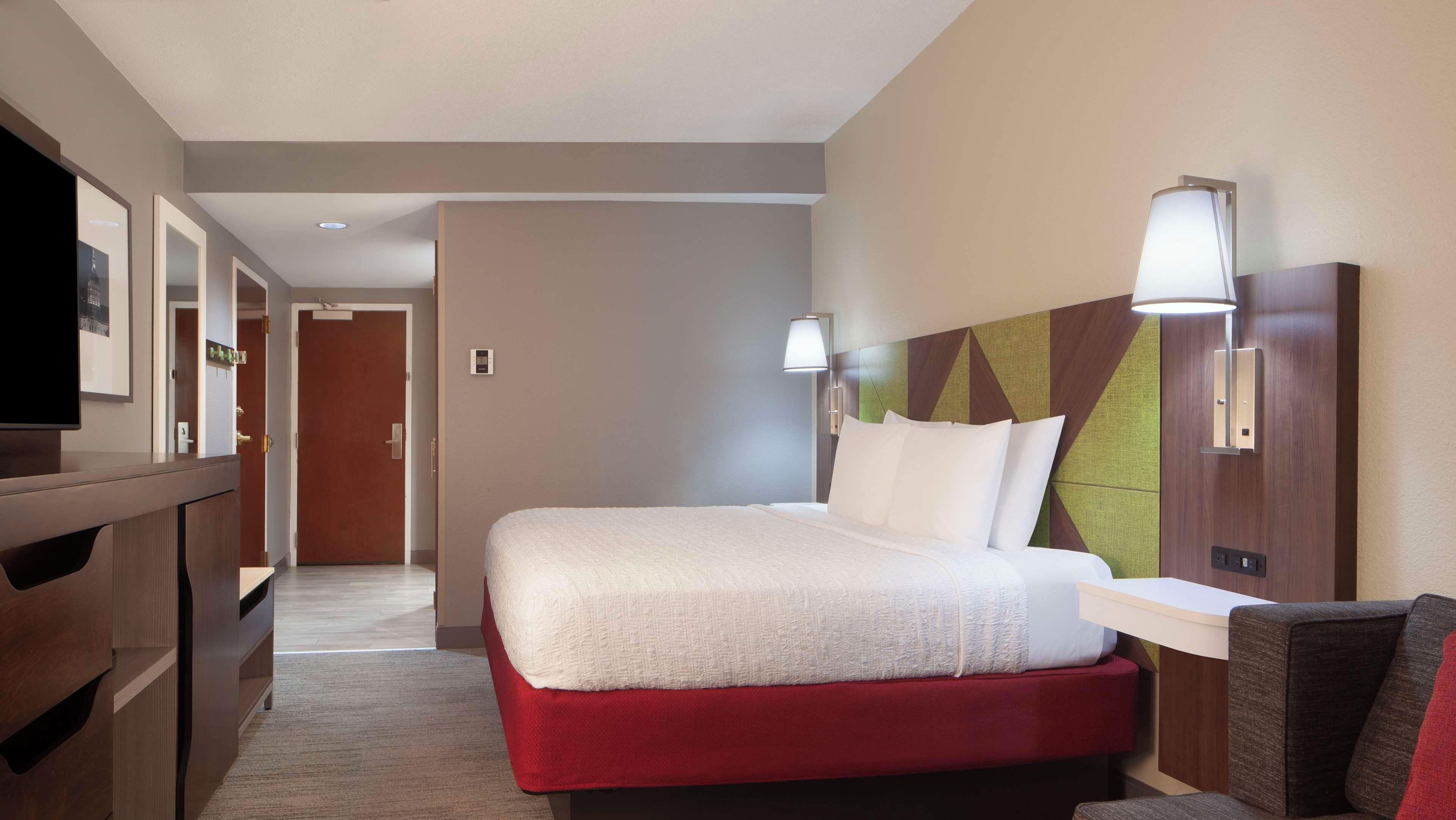 A hotel room with a bed, bedside table, lamp, and a television on a stand.
