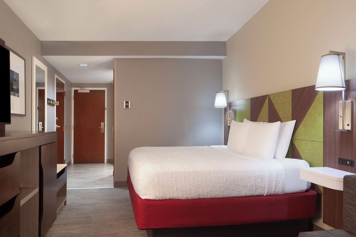 A hotel room with a bed, a desk, a chair, and a television.
