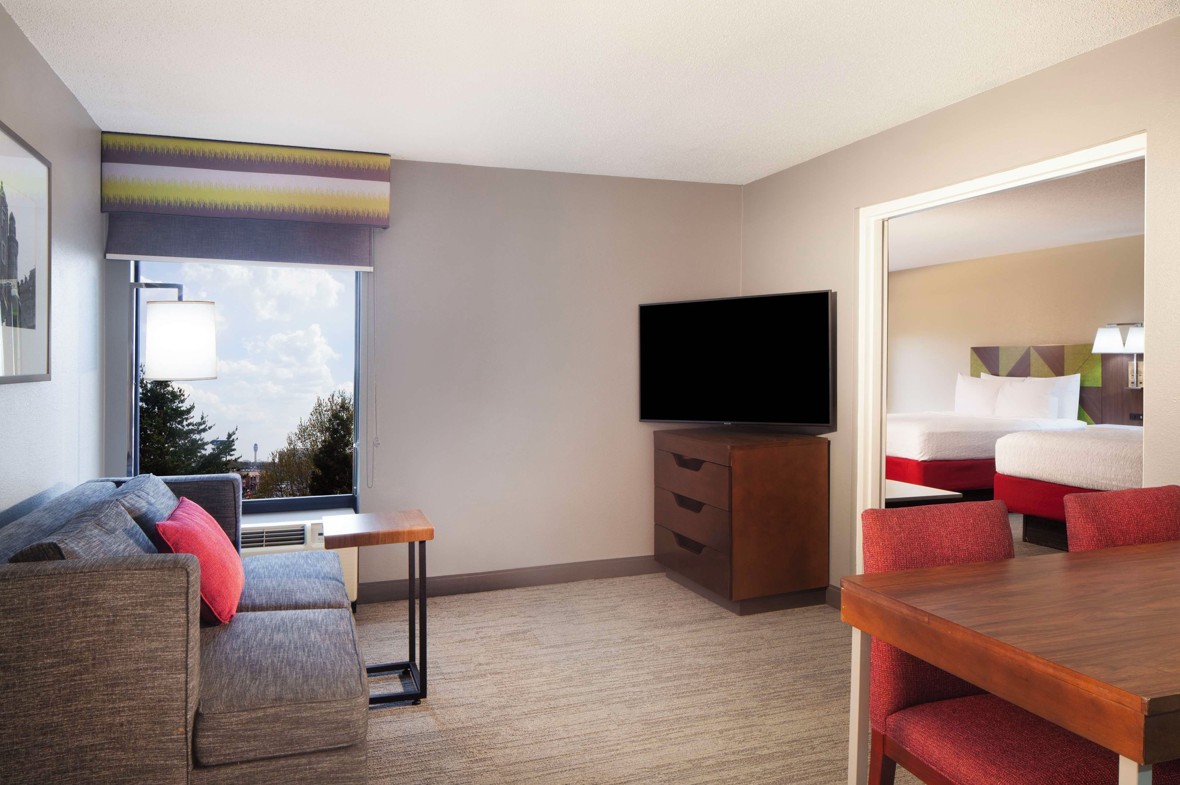 A hotel room with a sofa, a TV, a wooden table, and a bed with red and white bedding.