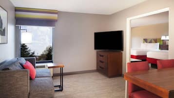 Een hotelkamer met een bank, een televisie, een bureau en een eettafel.