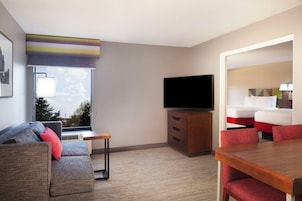 Una habitación de hotel con sofá, televisión, escritorio y mesa de comedor.