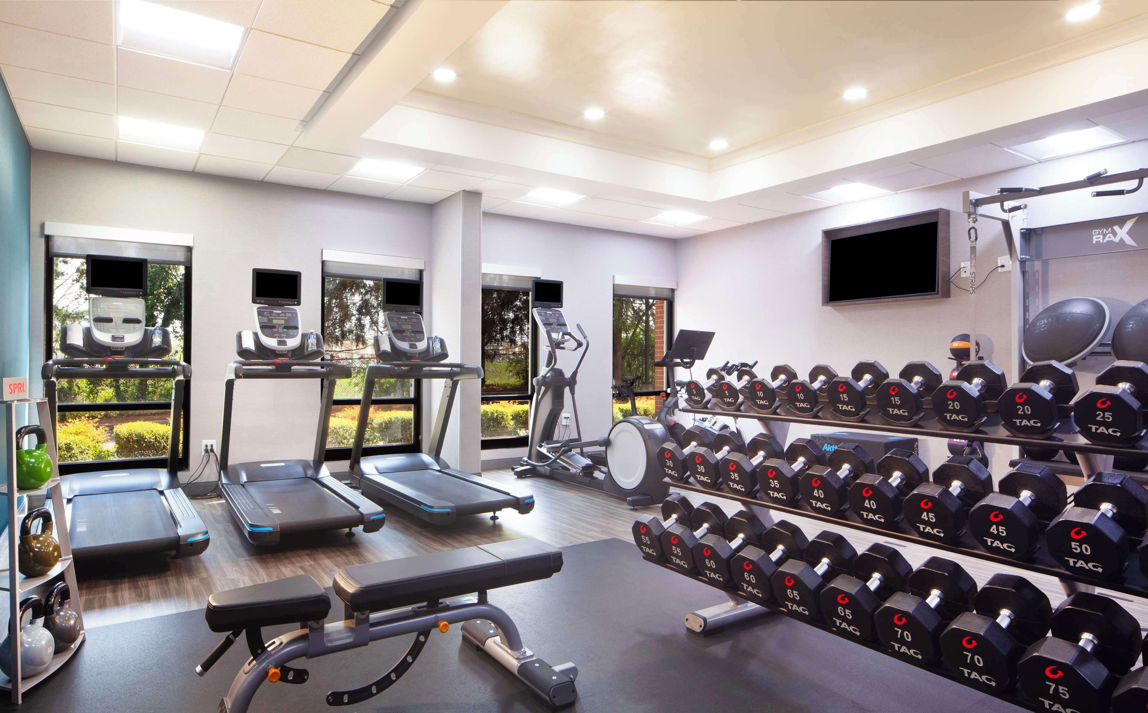Une salle de sport équipée de tapis de course, de vélos elliptiques, d’un banc de développé couché et d’une série de haltères.