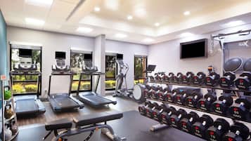 Une salle de sport équipée de tapis de course, de vélos elliptiques, d’un banc de développé couché et d’une série de haltères.