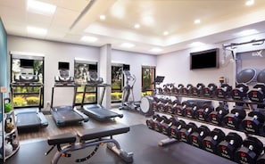 Ett gym med löpband, crosstrainers, en bänkpress och ett ställ med hantlar.
