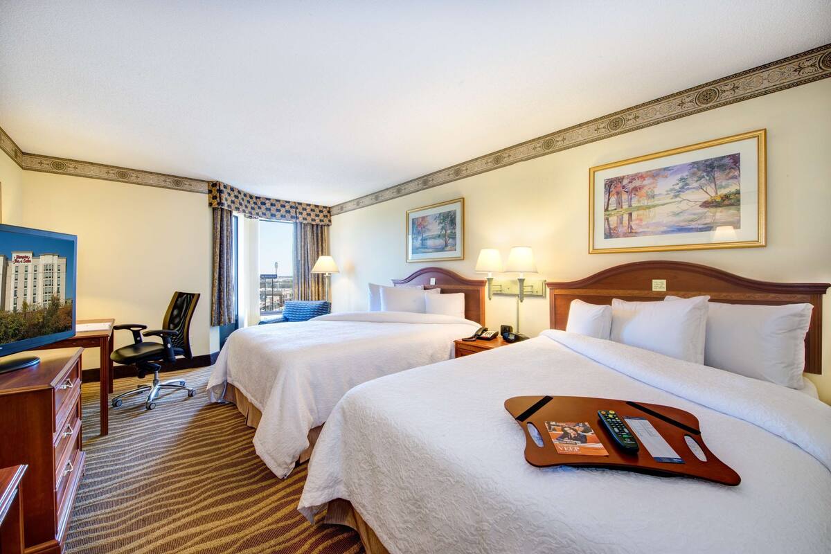 A hotel room with two beds, a desk, a chair, and a TV.