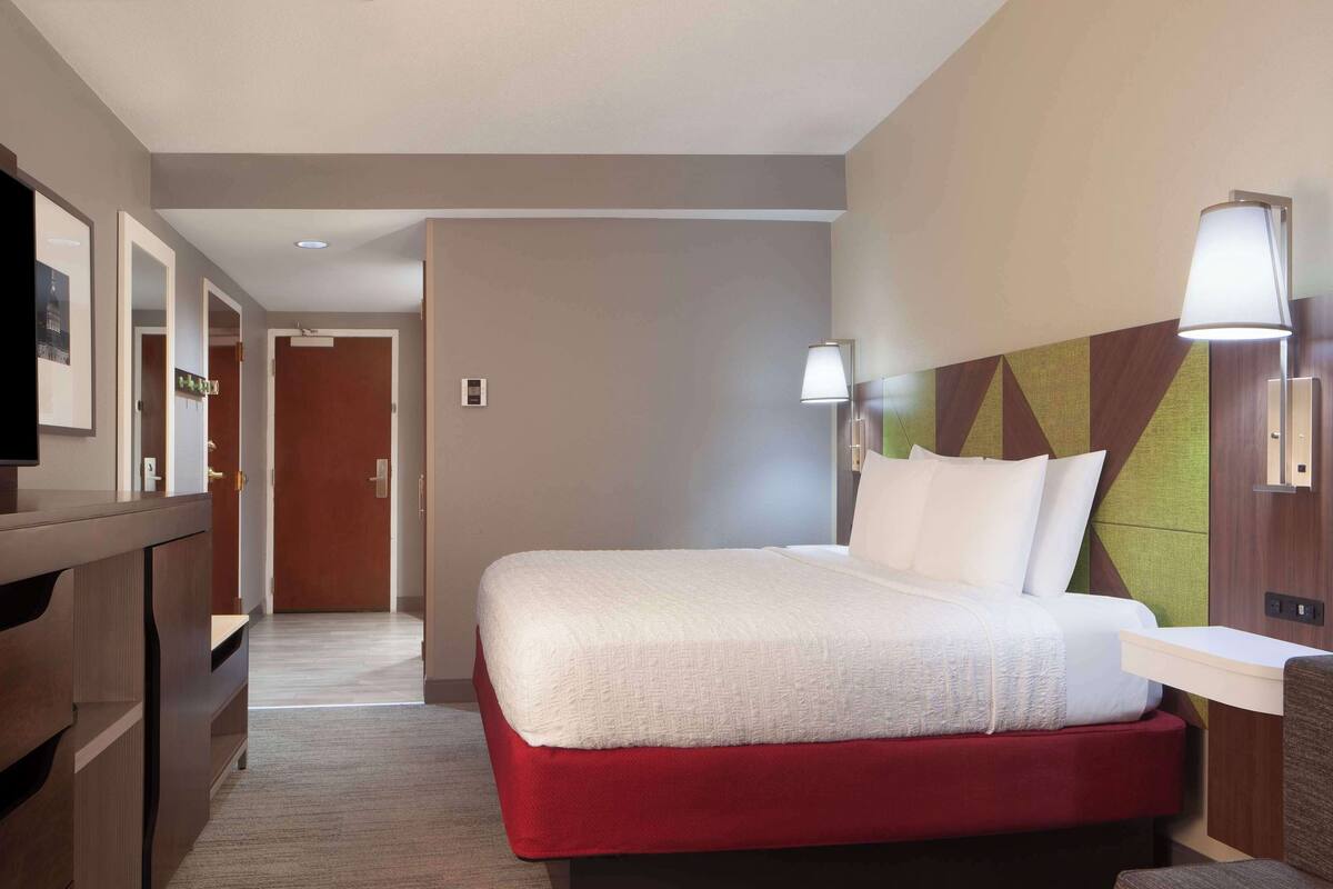 A hotel room with a bed, a desk, a chair, and a television.