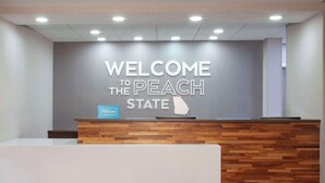 A reception desk with a "Welcome to the Peach State" sign, a Hilton logo, and a wooden panel design. - Hampton Inn & Suites Atlanta Airport North I-85 (Atlanta)