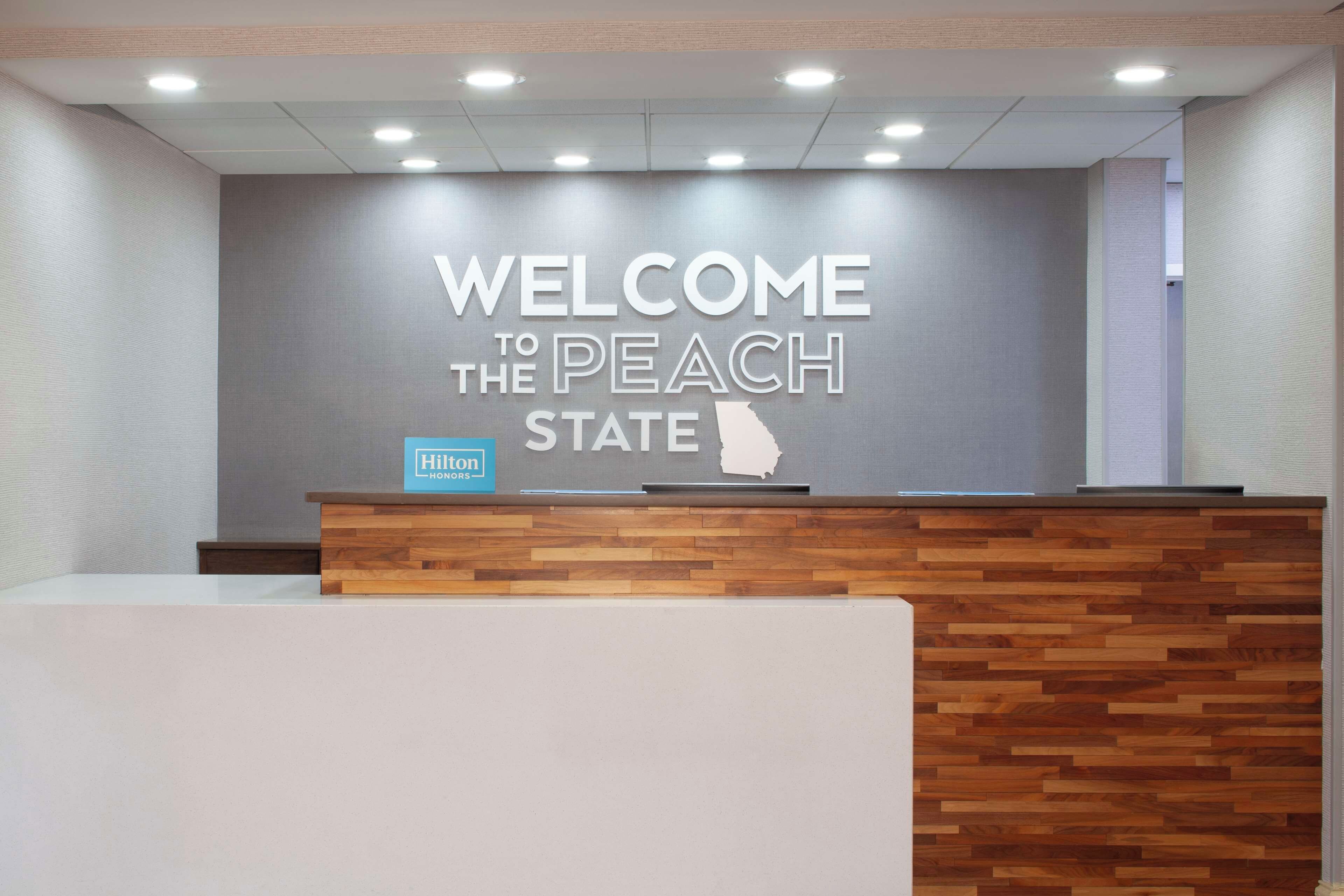Ein Empfangsschalter mit einem Schild, auf dem 'Welcome to the Peach State' steht, dem Hilton-Logo und einem Holzpaneel-Design.