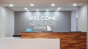 A reception desk with a 'WELCOME TO THE PEACH STATE' sign above it. - Hampton Inn & Suites Atlanta Airport North I-85 (Atlanta)