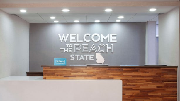A reception desk with a 'WELCOME TO THE PEACH STATE' sign above it. - Hampton Inn & Suites Atlanta Airport North I-85 (Atlanta)