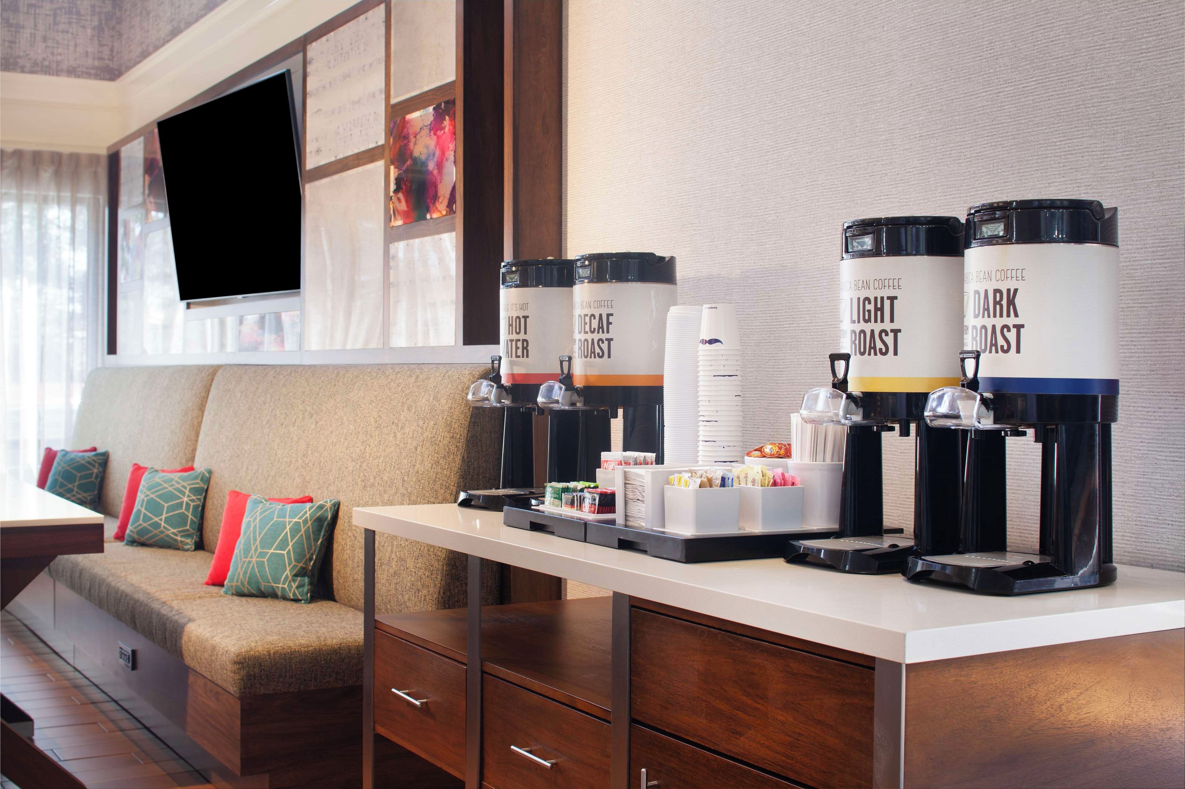 A hotel room with a sofa, a coffee station with decaf and light roast options, and a TV mounted on the wall.
