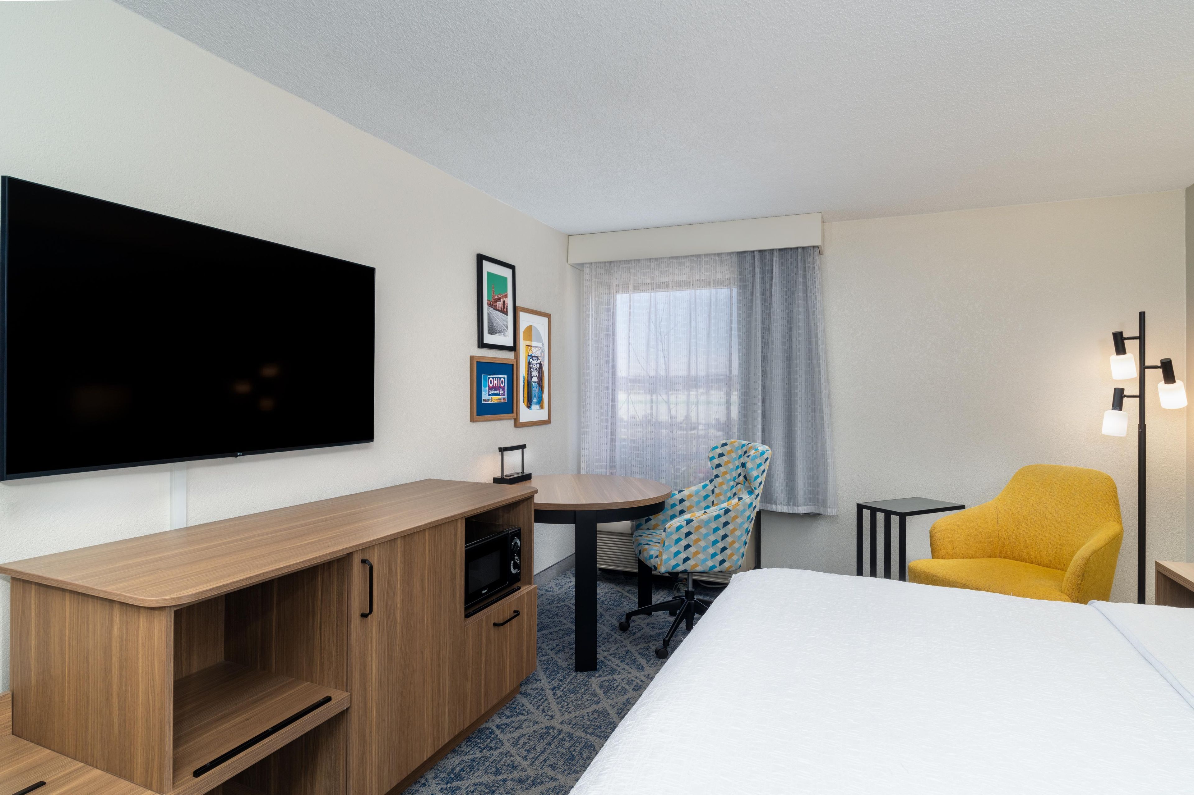 A hotel room with a bed, a desk, a chair, a TV, and a window with curtains.