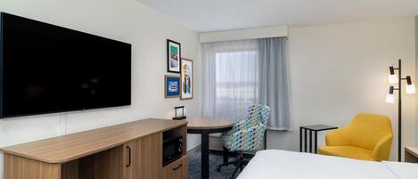 A hotel room with a bed, a desk, a chair, a TV, and a window with curtains.