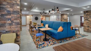 A modern interior with a blue sofa, wooden tables, and chairs, stone walls, and a patterned rug. - Hampton Inn Marietta (Marietta)