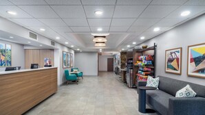 A hotel reception area with a wooden reception desk, a seating area with teal chairs, a sofa, and a small table. There are framed pictures on the walls and a display of various items on the right side. - Hampton Inn Marietta (Marietta)