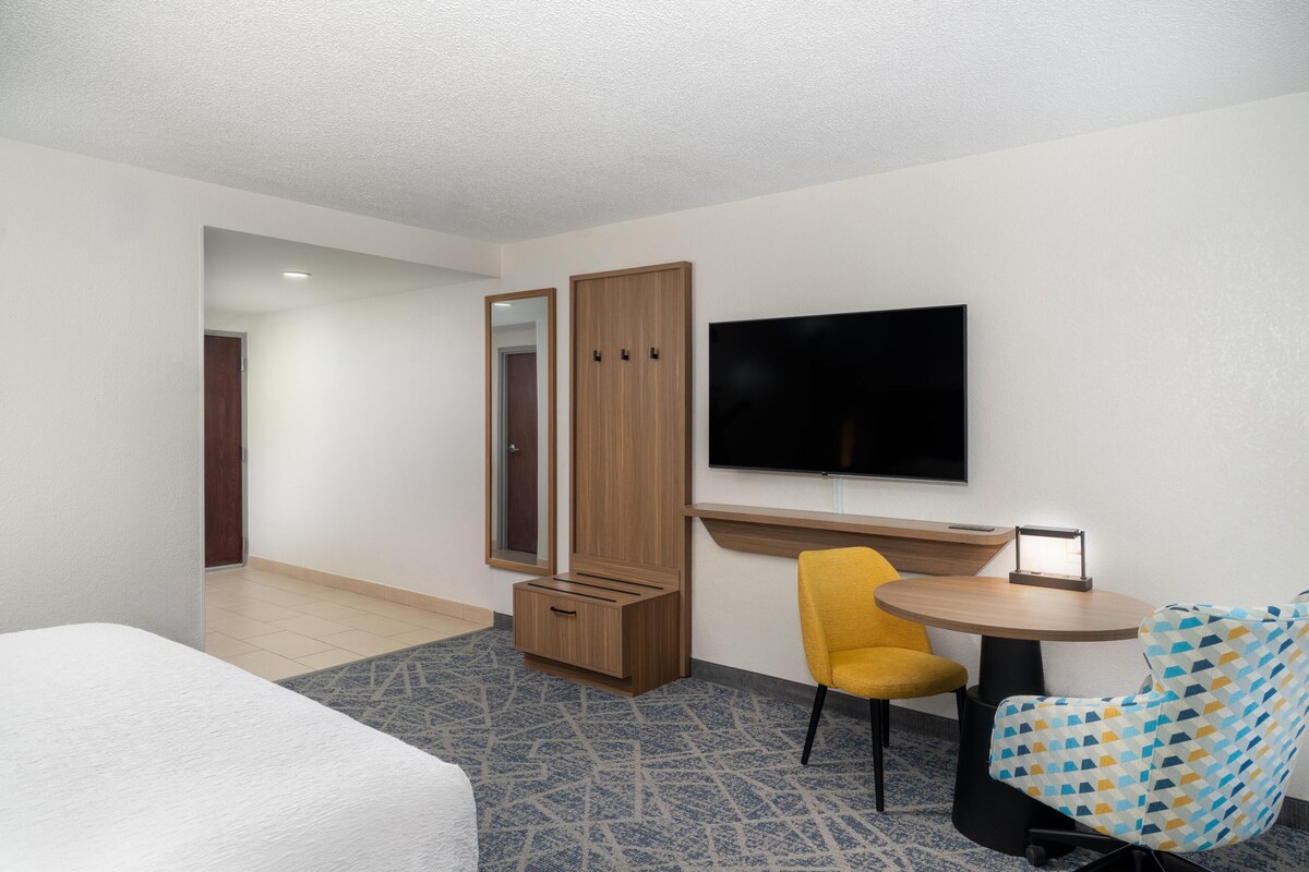 Ein Hotelzimmer mit einem Bett, einem Schreibtisch mit Stuhl, einem Fernseher und einem Kleiderschrank.