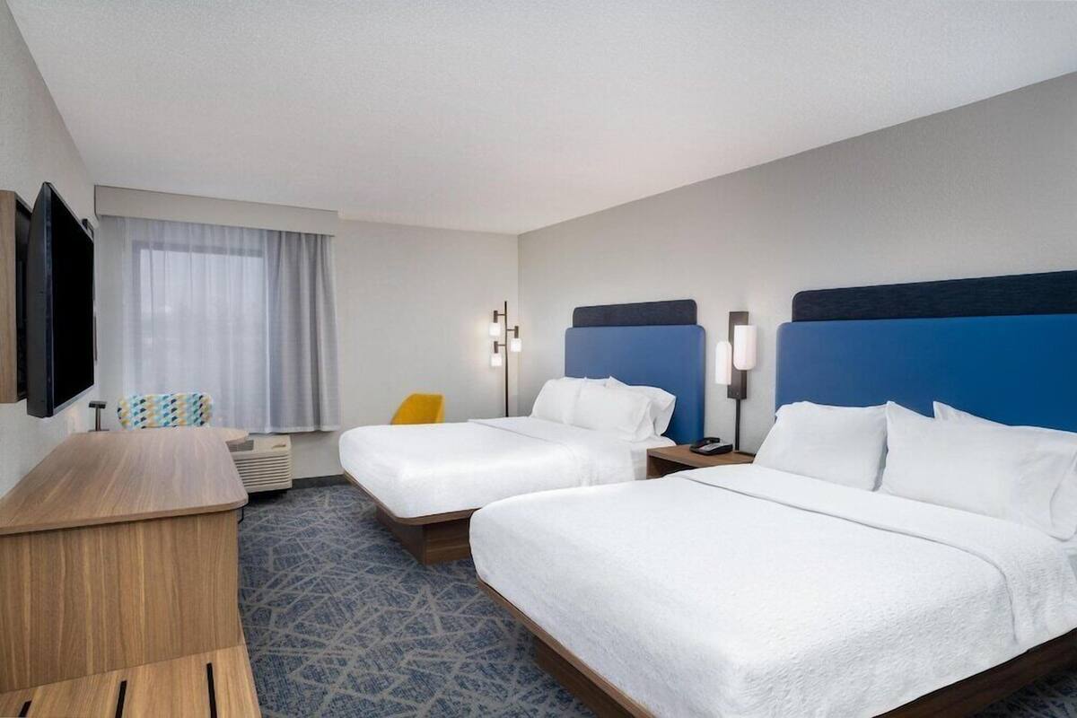 A hotel room with two beds, a desk, a TV, and a window with curtains.