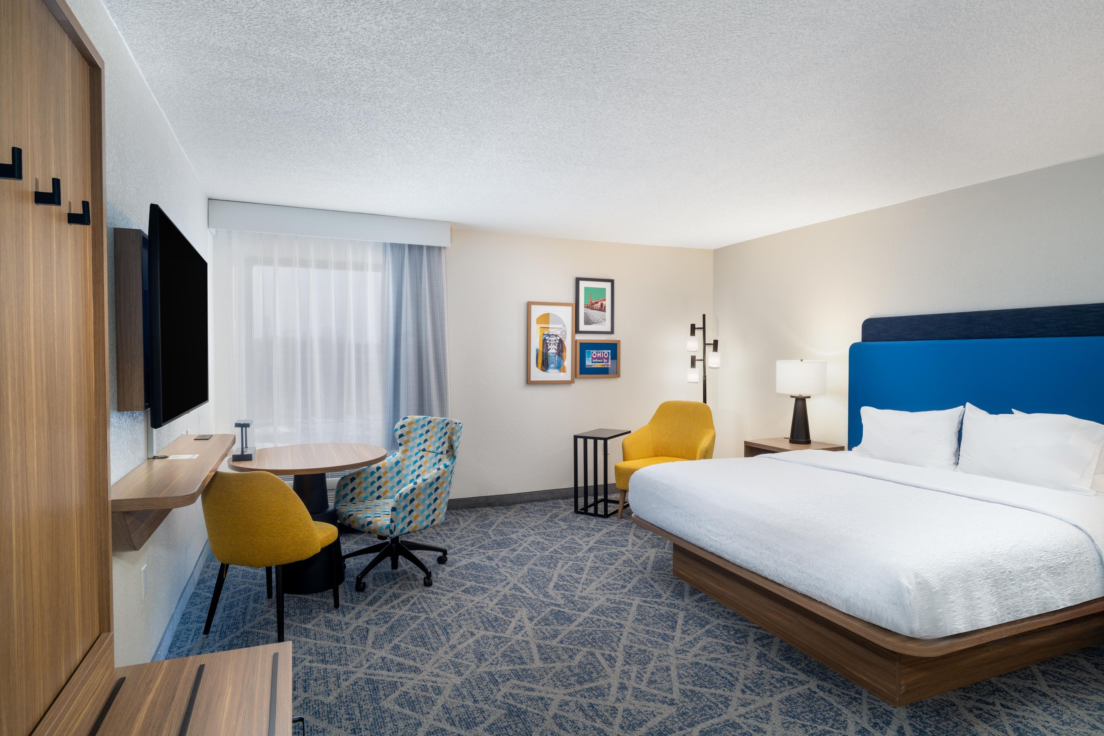 A hotel room with a bed, a desk, a chair, a television, and a window with curtains.
