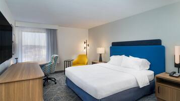Quarto de hotel com uma cama grande, escrivaninha, cadeira, abajur e televisão.