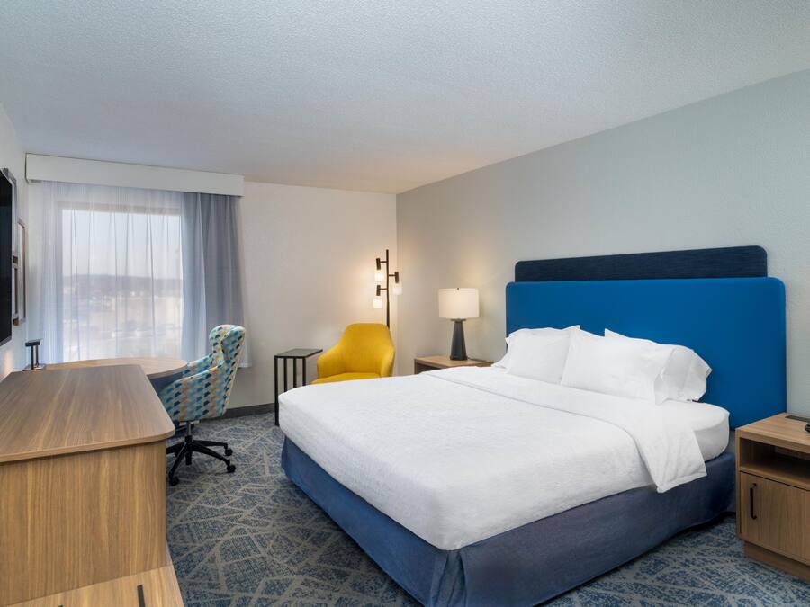 Quarto de hotel com uma cama grande, escrivaninha, cadeira, abajur e televisão.