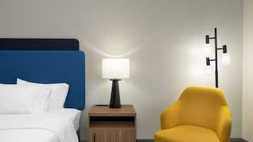 A hotel room with a bed, a bedside table with a lamp, a small wooden cabinet, and a yellow armchair.
