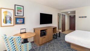 A hotel room with a bed, a TV mounted on the wall, a small wooden table with a microwave, a patterned armchair, and framed pictures on the wall. - Hampton Inn Marietta (Marietta)