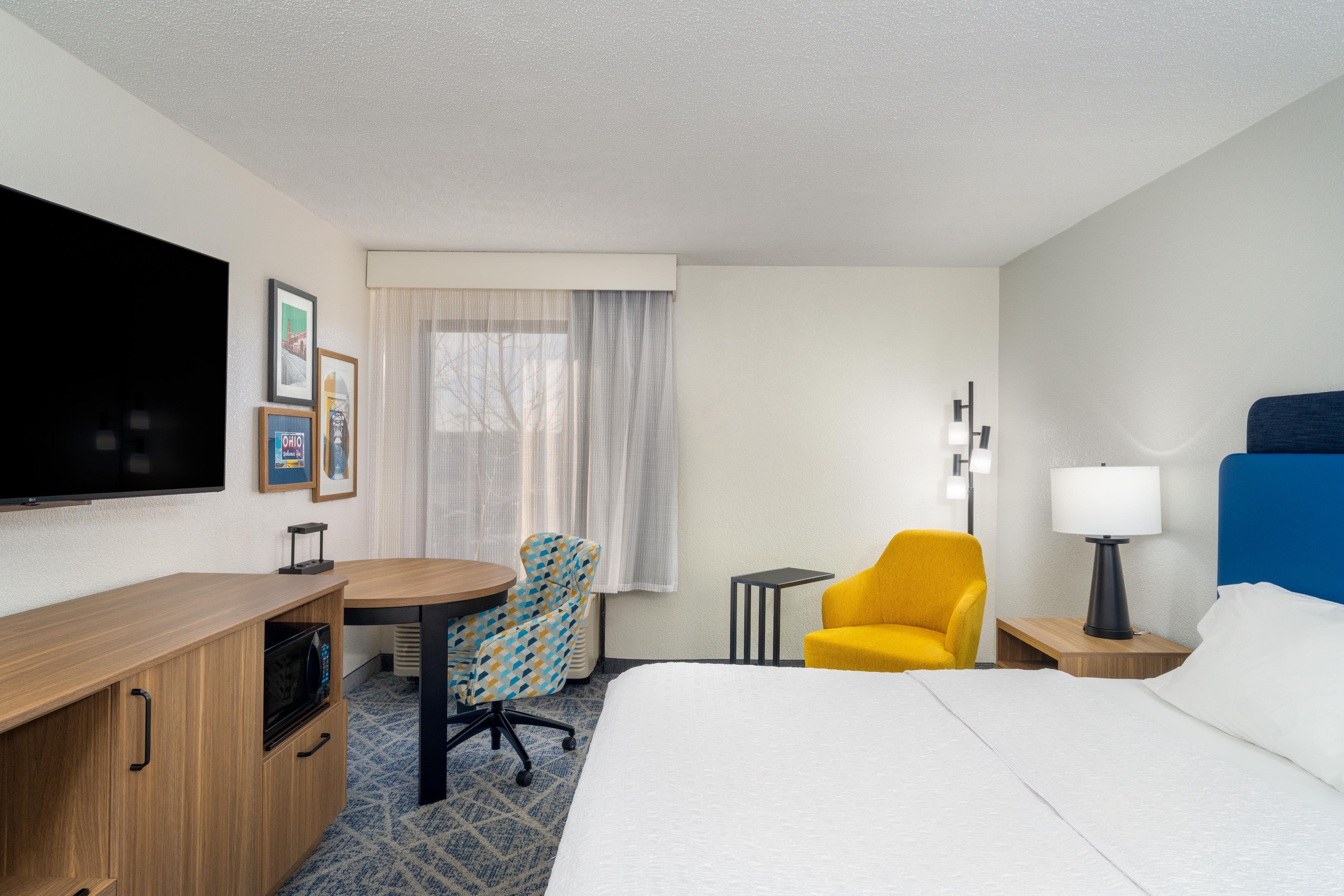 A hotel room with a bed, a desk, a chair, a television, and a window with curtains.